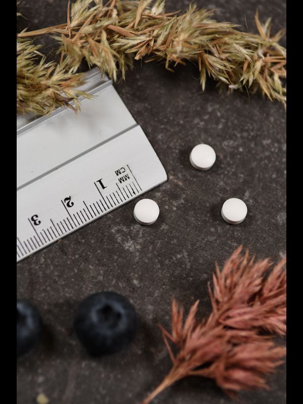 Nahaufnahme von weißen Tabletten neben einem Lineal und Dekoration. Tabletten sind rund und klein. Hintergrund dunkel.