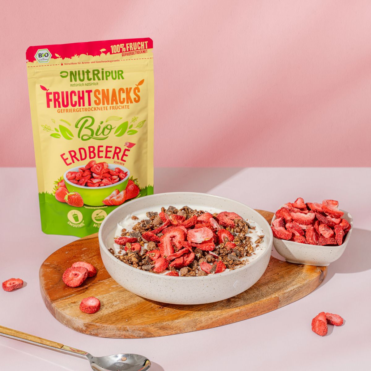 Schale mit Joghurt und gefriergetrockneten Erdbeeren. Daneben eine Packung NutriPur Erdbeeren und eine Schale mit Erdbeeren.