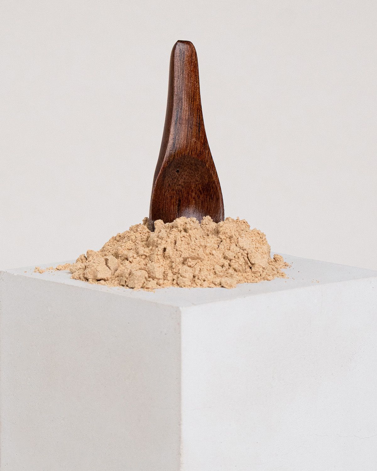 Holzlöffel steckt in Maca-Pulver. Pulver auf weißem Podest.
