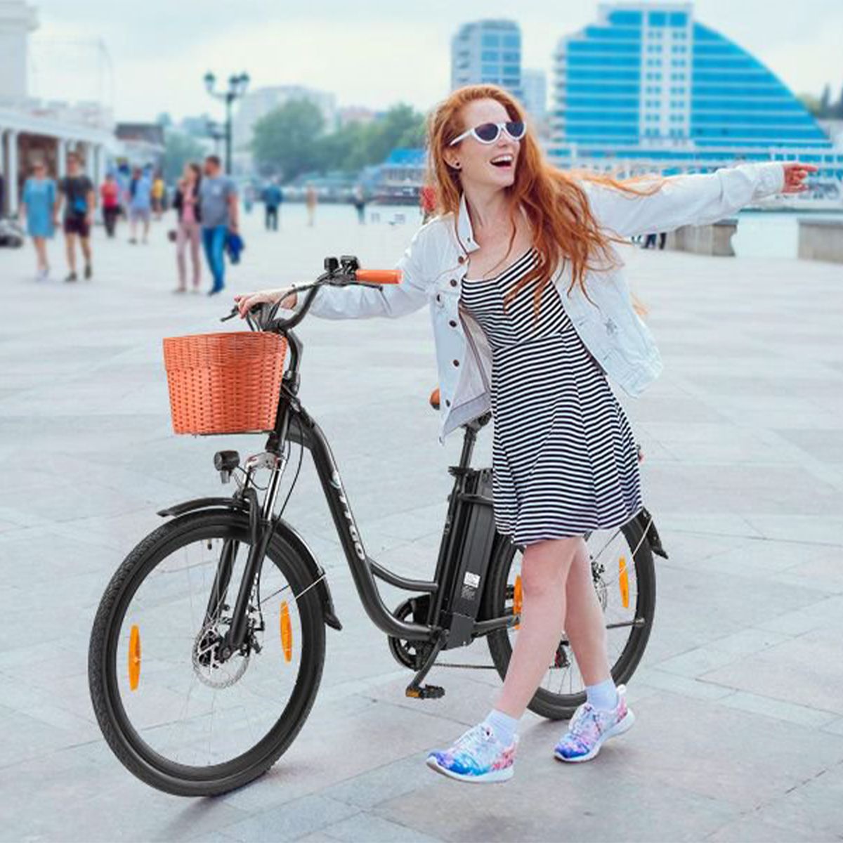 Frau mit Elektrofahrrad. Schwarzes Fahrrad mit Korb, braunem Sattel und orangefarbenen Griffen. TTGO.