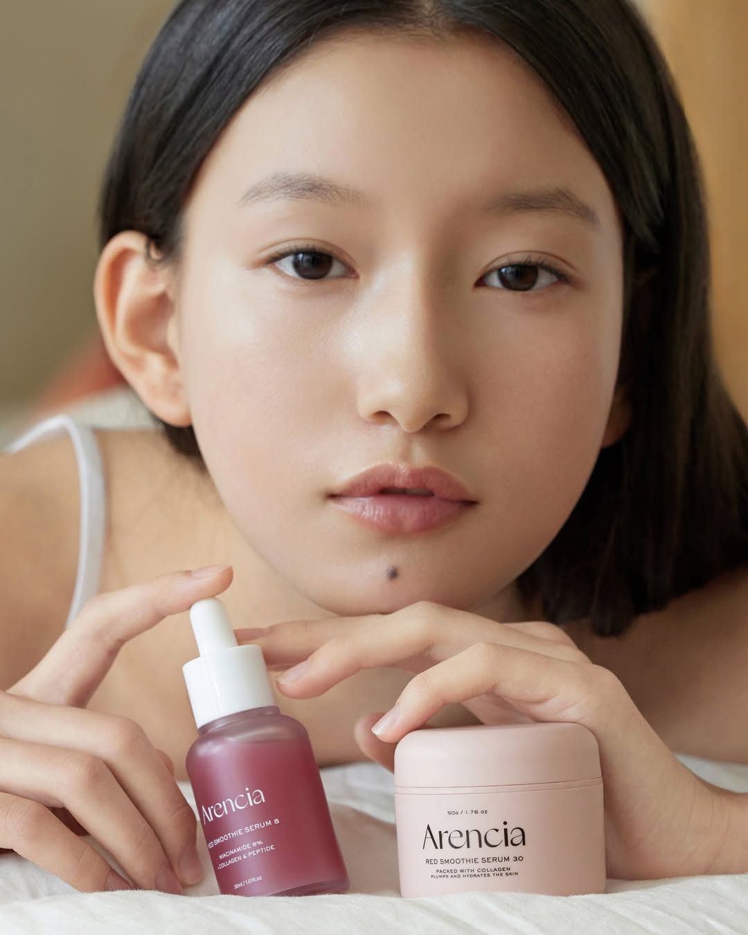 Junge Frau hält zwei Produkte. ARENCIA Red Smoothie Serum 8 Flasche und Cremebehälter. Aufschrift sichtbar.