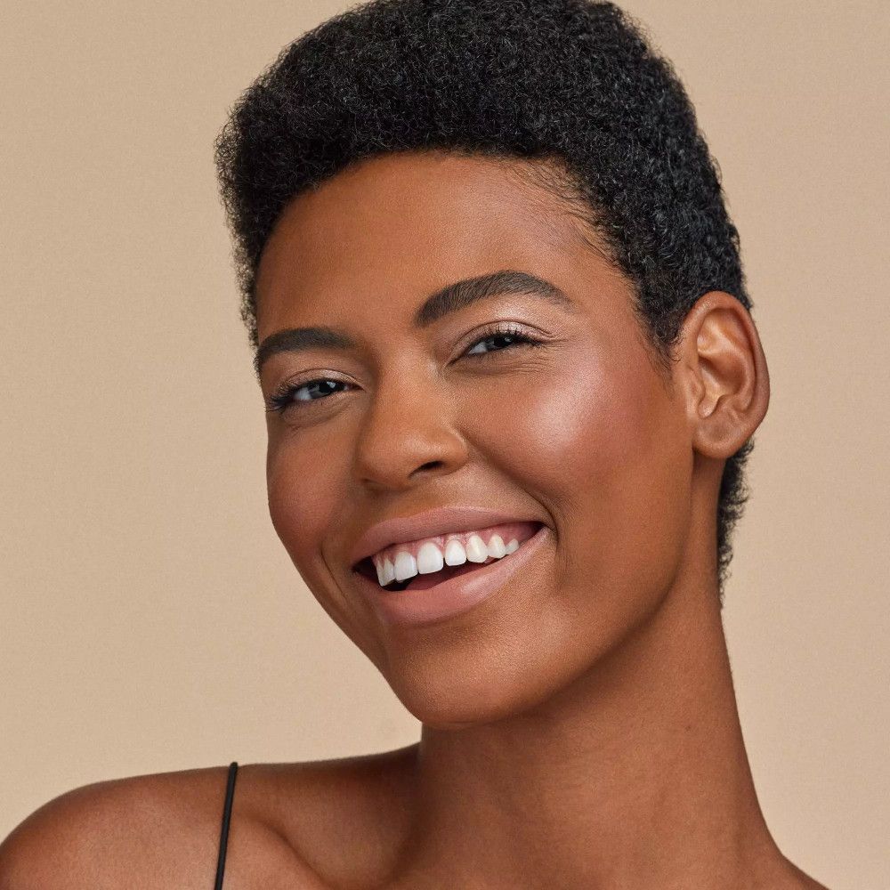 Porträt einer Frau mit gebräunter Haut. Aufgetragenes Produkt auf Wangen und Stirn. Natürliches Make-up.