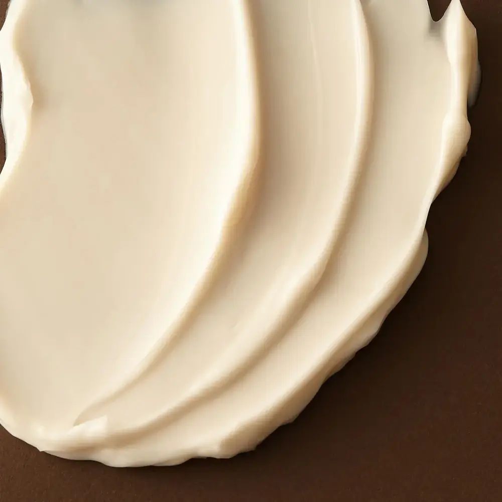 Nahaufnahme von cremiger, weißer Creme auf braunem Hintergrund. Creme in Wellenform aufgetragen.