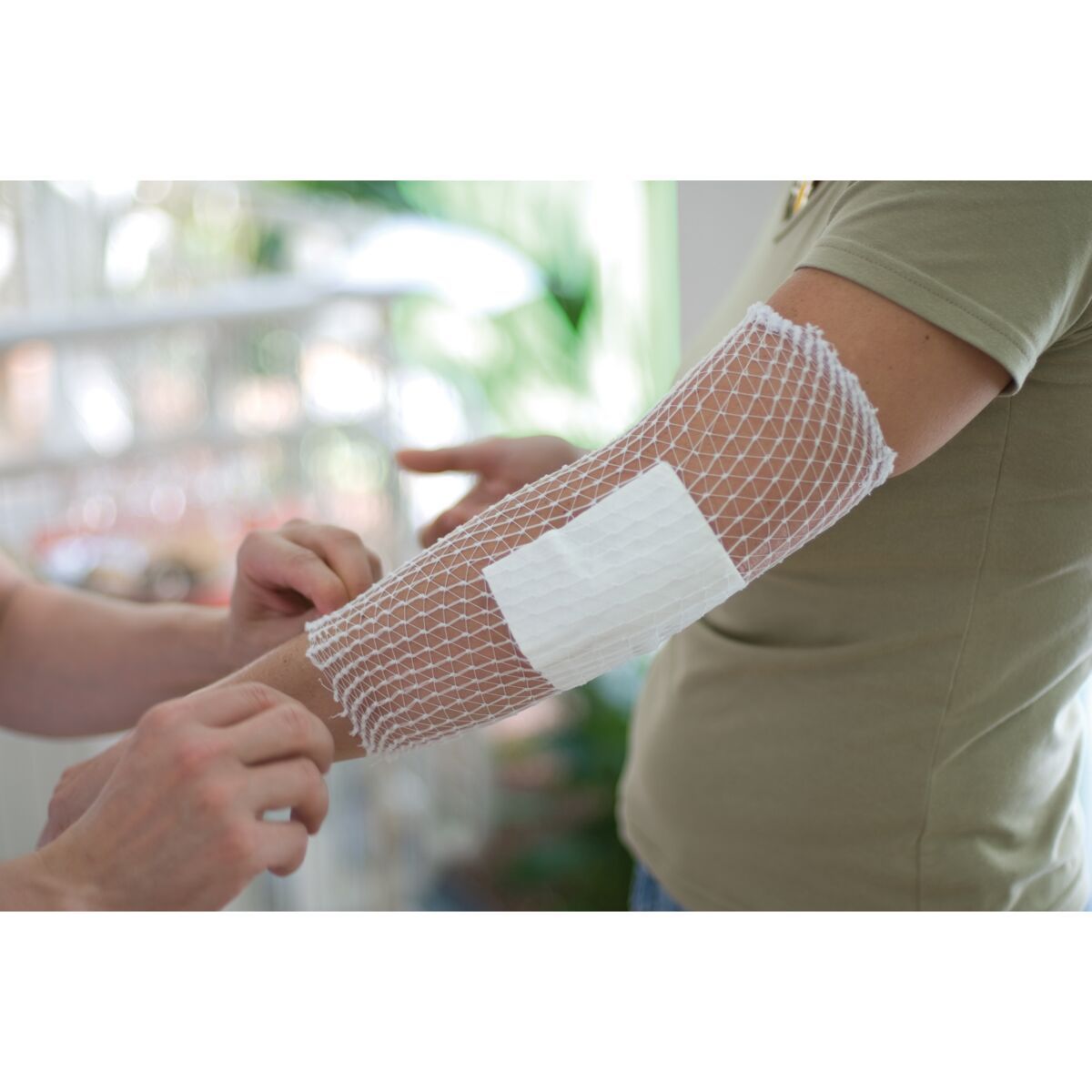 Weronet Netzverband wird auf einem Arm angelegt, mit einer Kompresse darunter.