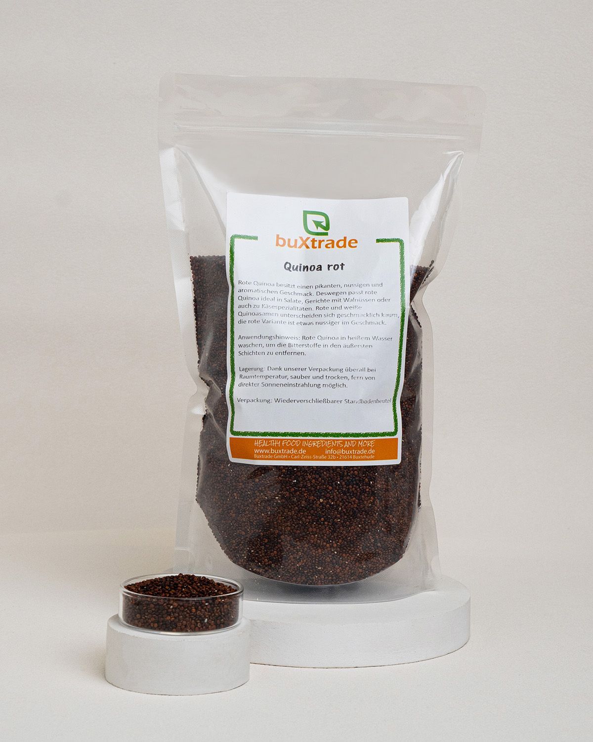 Transparente Tüte mit rotem Quinoa. Aufkleber mit Produktinformationen und Markenlogo buXtrade. Kleines Schälchen mit Quinoa daneben.