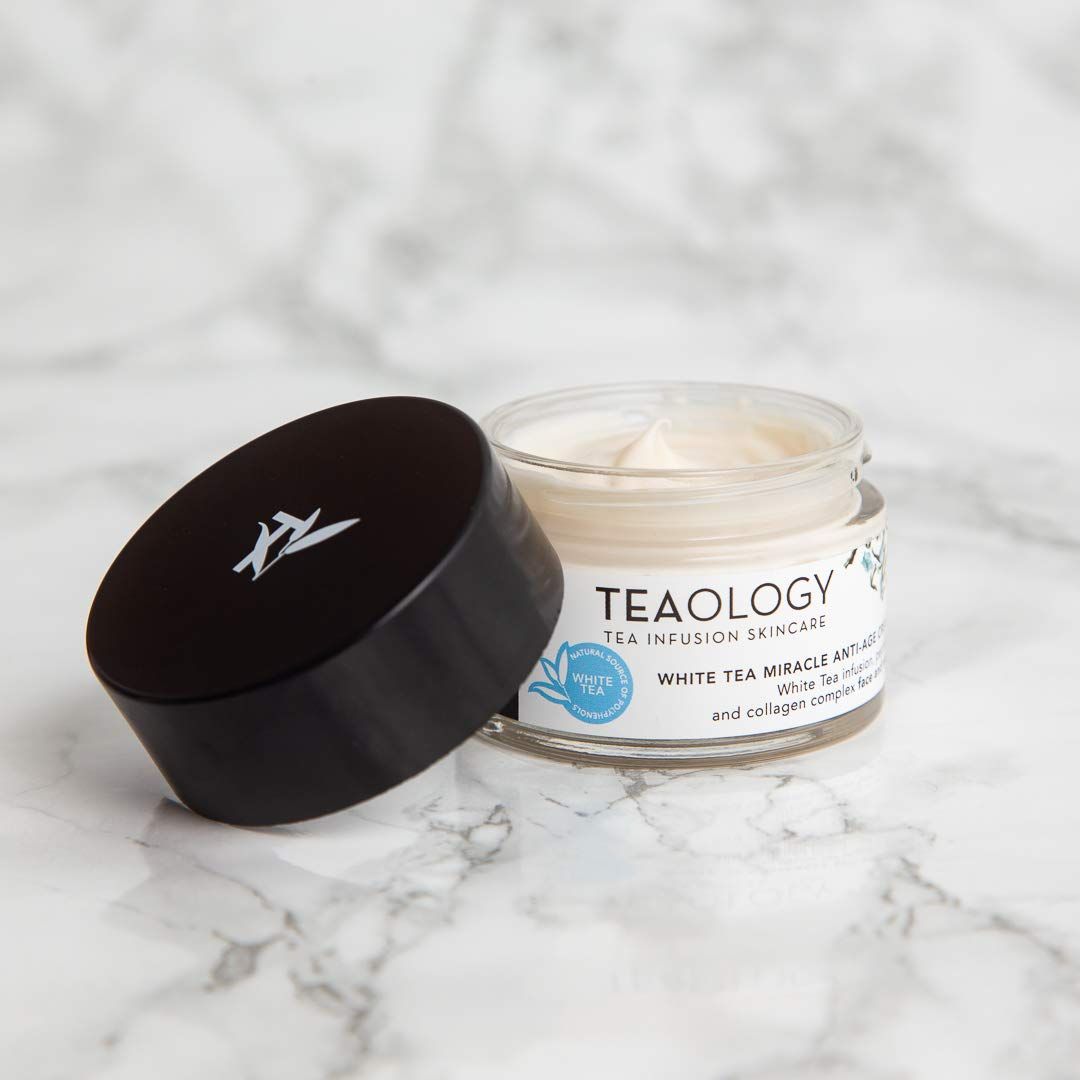 Creme in einem Glasbehälter mit offenem Deckel. Auf dem Etikett steht "Teaology" und "White Tea Miracle Anti-Age Cream".