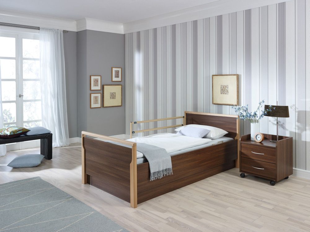 Bett mit Holzrahmen. Matratze, Kissen, Decke. Nachttisch mit Schubladen. In einem Raum mit Fenster.