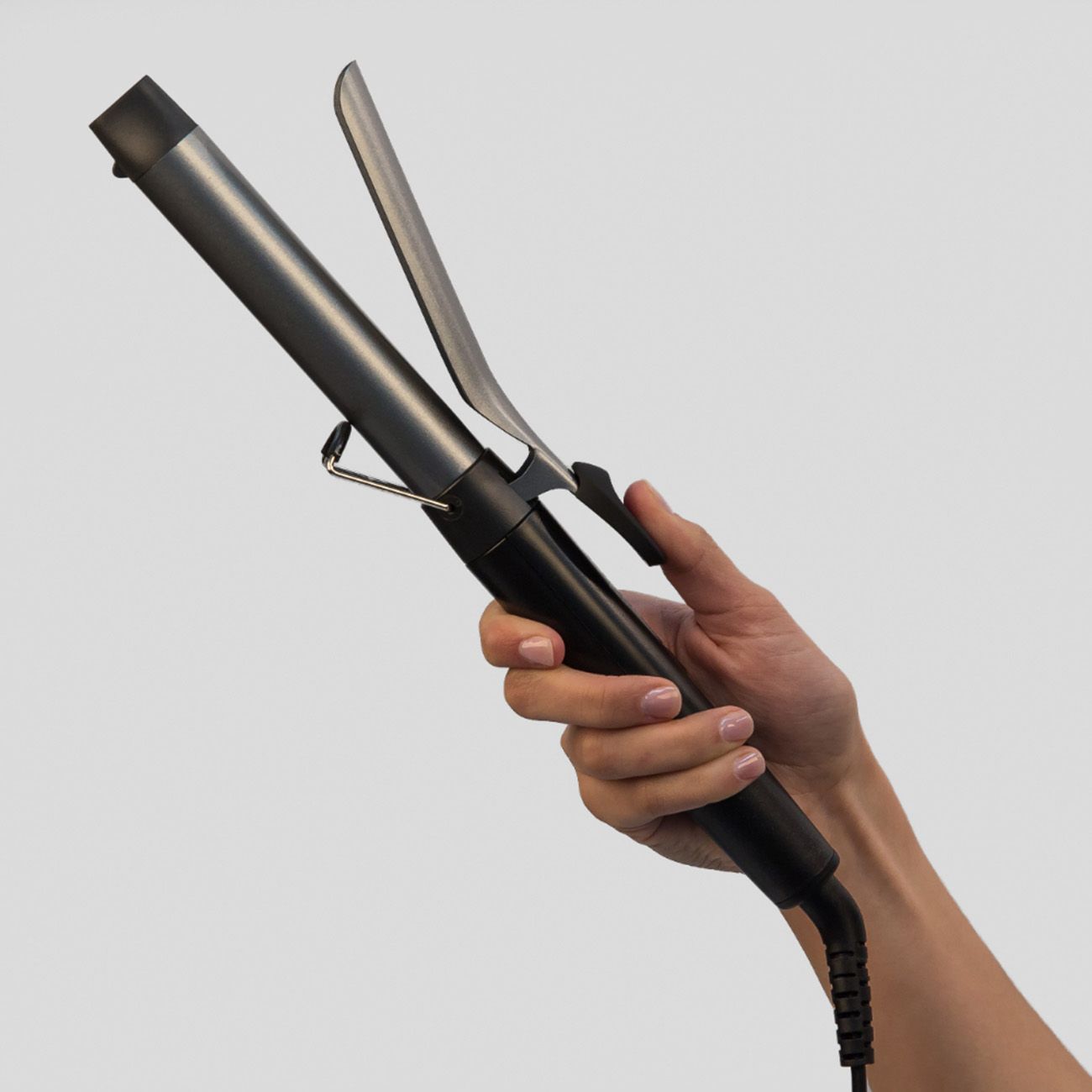 Lockenstab in Hand gehalten. Silberfarbener Stab, schwarzer Griff. Sichtbare Klammer.