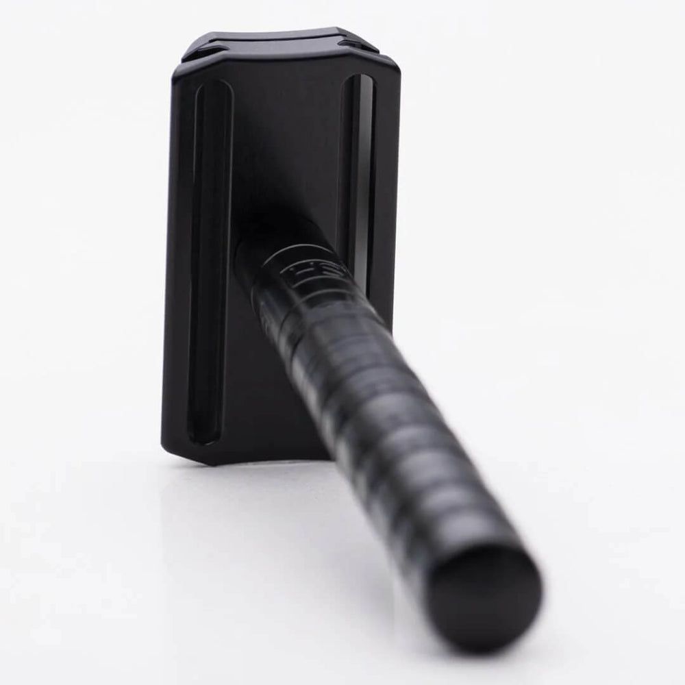 Schwarzer Rasierer, schräge Ansicht. Griff mit Rillen. Kopf oben.