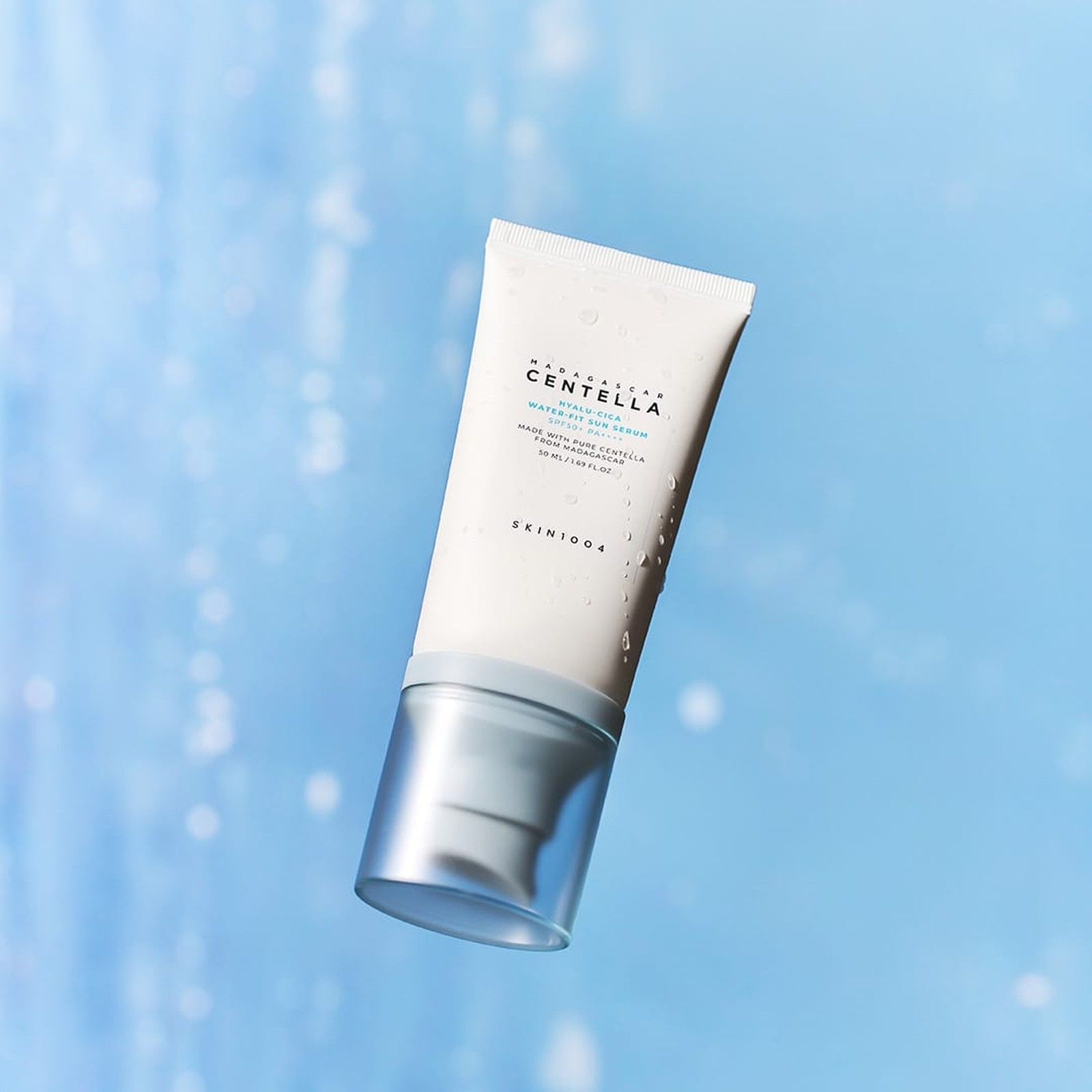 SKIN1004 Hyalu-Cica Water-Fit Sonnenserum SPF 50+ PA++++ schwebt vor einem verschwommenen blauen Hintergrund.