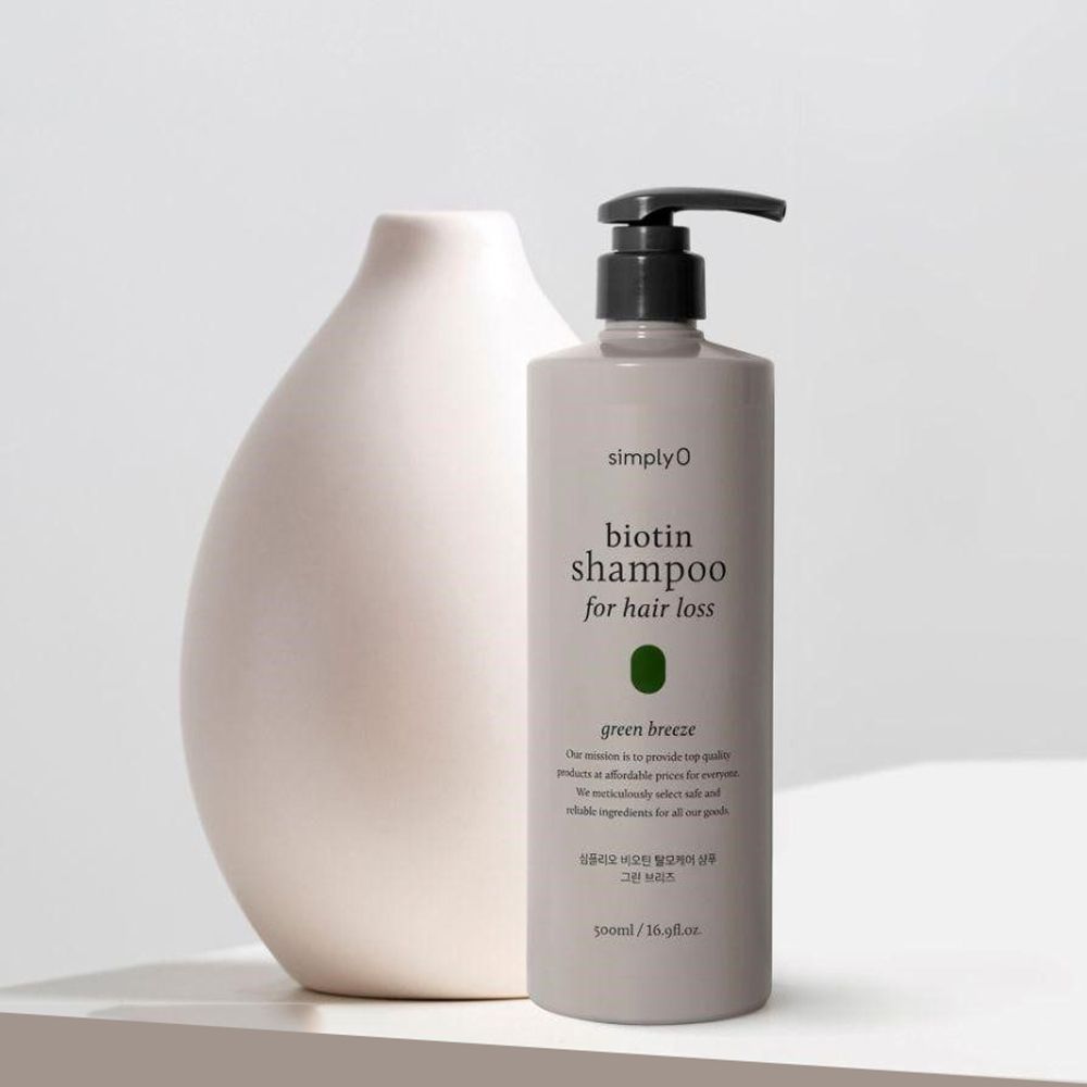Graue Shampoo-Flasche mit schwarzem Pumpkopf. Beschriftung: Biotin Shampoo for hair loss, Green Breeze. Steht neben einer Vase.