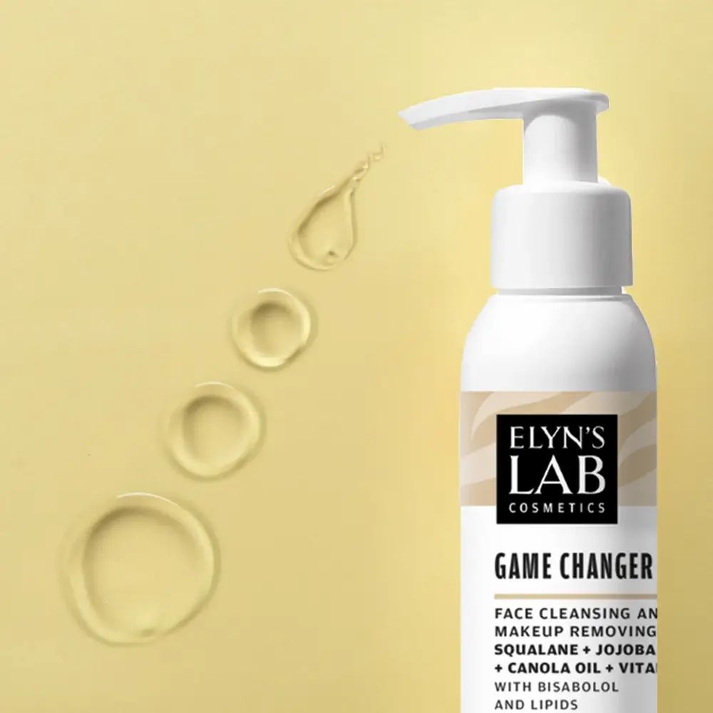Weiße Flasche mit Pumpe. Etikett mit Produktnamen und Inhaltsstoffen. Daneben Öltropfen. Text: Game Changer, Face Cleansing, Squalane, Jojoba.