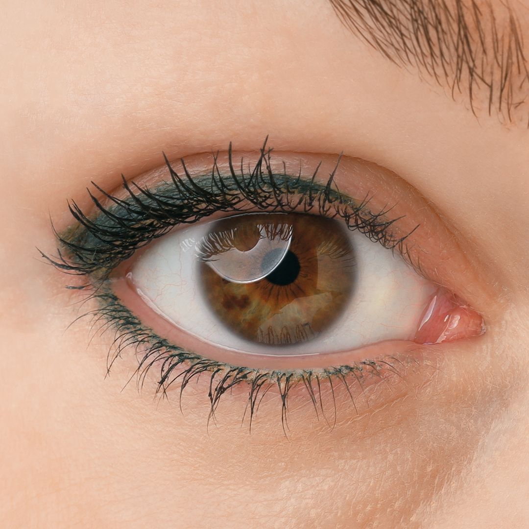 Nahaufnahme eines Auges mit dunkelgrünem Kajal-Eyeliner. Eine Kontaktlinse ist im Auge sichtbar.