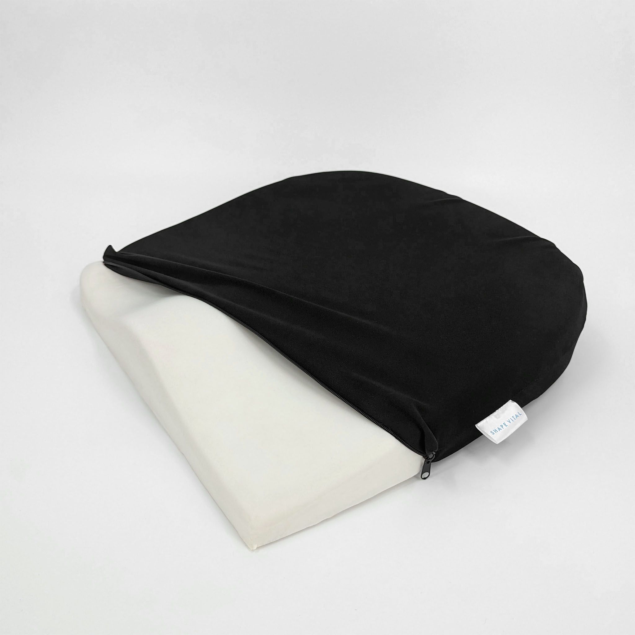 Keilförmiges Sitzkissen, schwarzer Bezug geöffnet. Schaumstoffkern sichtbar. Reißverschluss.