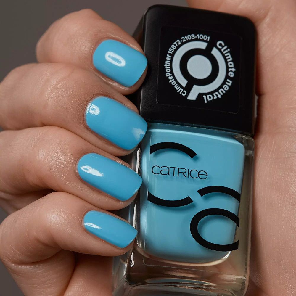 Helle blaue Fingernägel und Nagellackflasche. Auf der Flasche steht Catrice und ein Logo. Climate Partner.
