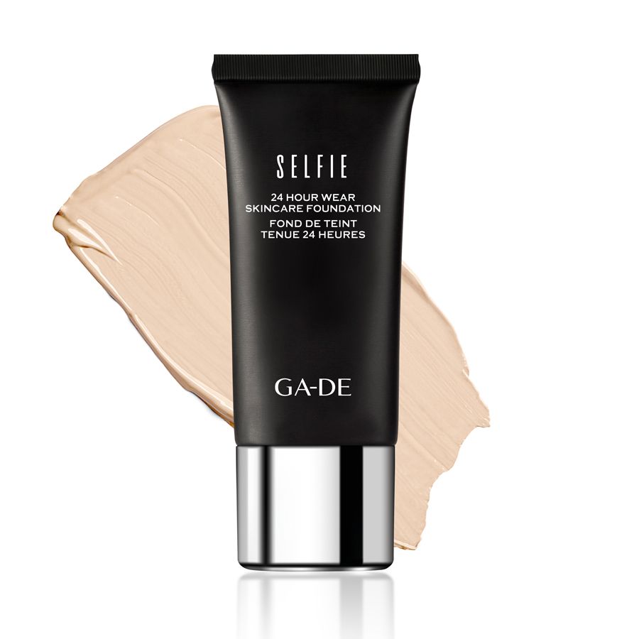 Schwarze Tube mit GA-DE Logo und 'SELFIE 24 HOUR WEAR SKINCARE FOUNDATION' Aufschrift. Daneben ein Swatch hellbrauner Foundation.