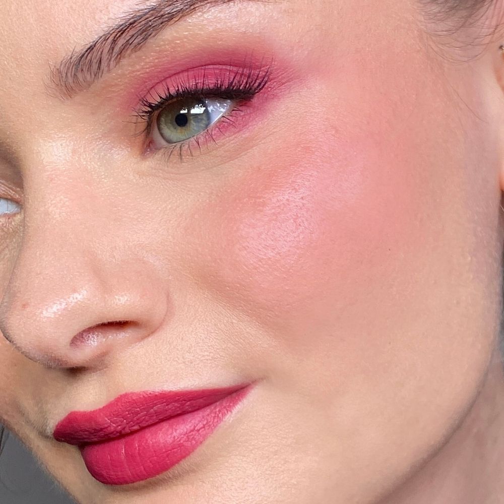Nahaufnahme eines Gesichts mit rosa Make-up. Rosa Lidschatten, Rouge und Lippenstift. Grünes Auge.