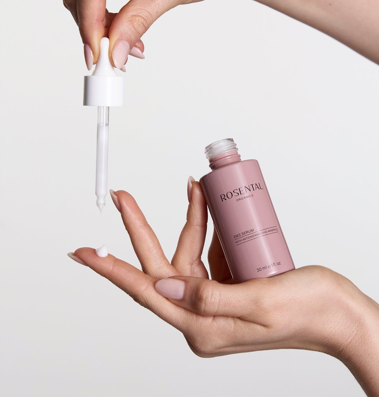 Hände halten Flasche und Pipette. Serum tropft auf die Hand. Rosa Flasche, weißer Deckel.