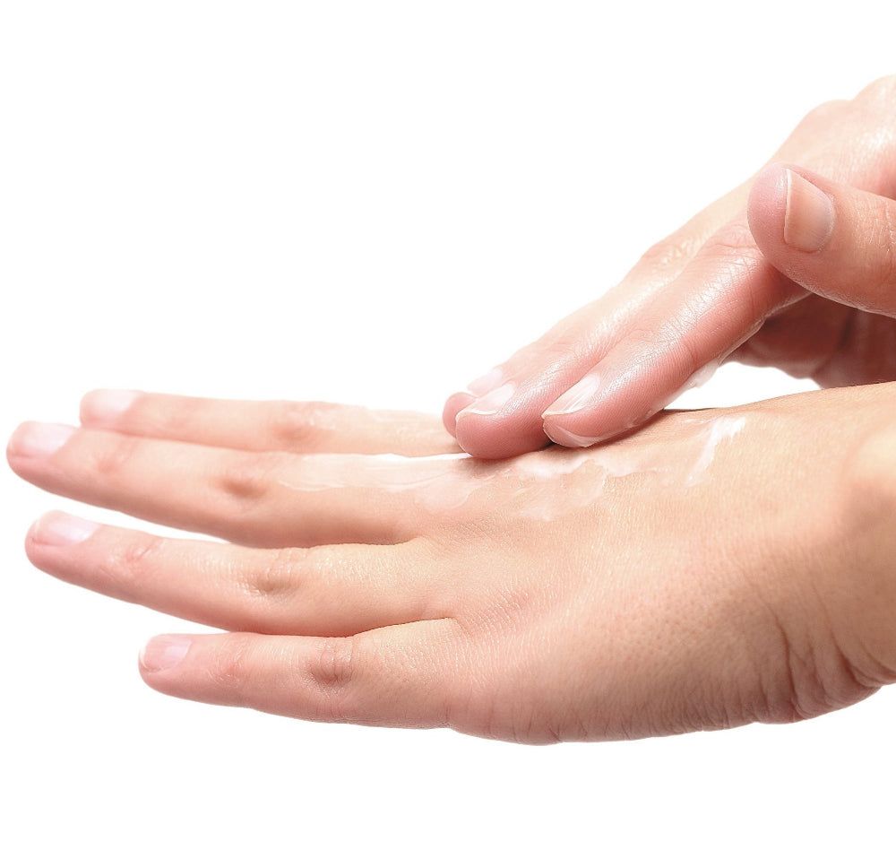 Hände, eine Handfläche mit Creme, eine andere Hand verteilt die Creme. Hautfarben, weißer Hintergrund.