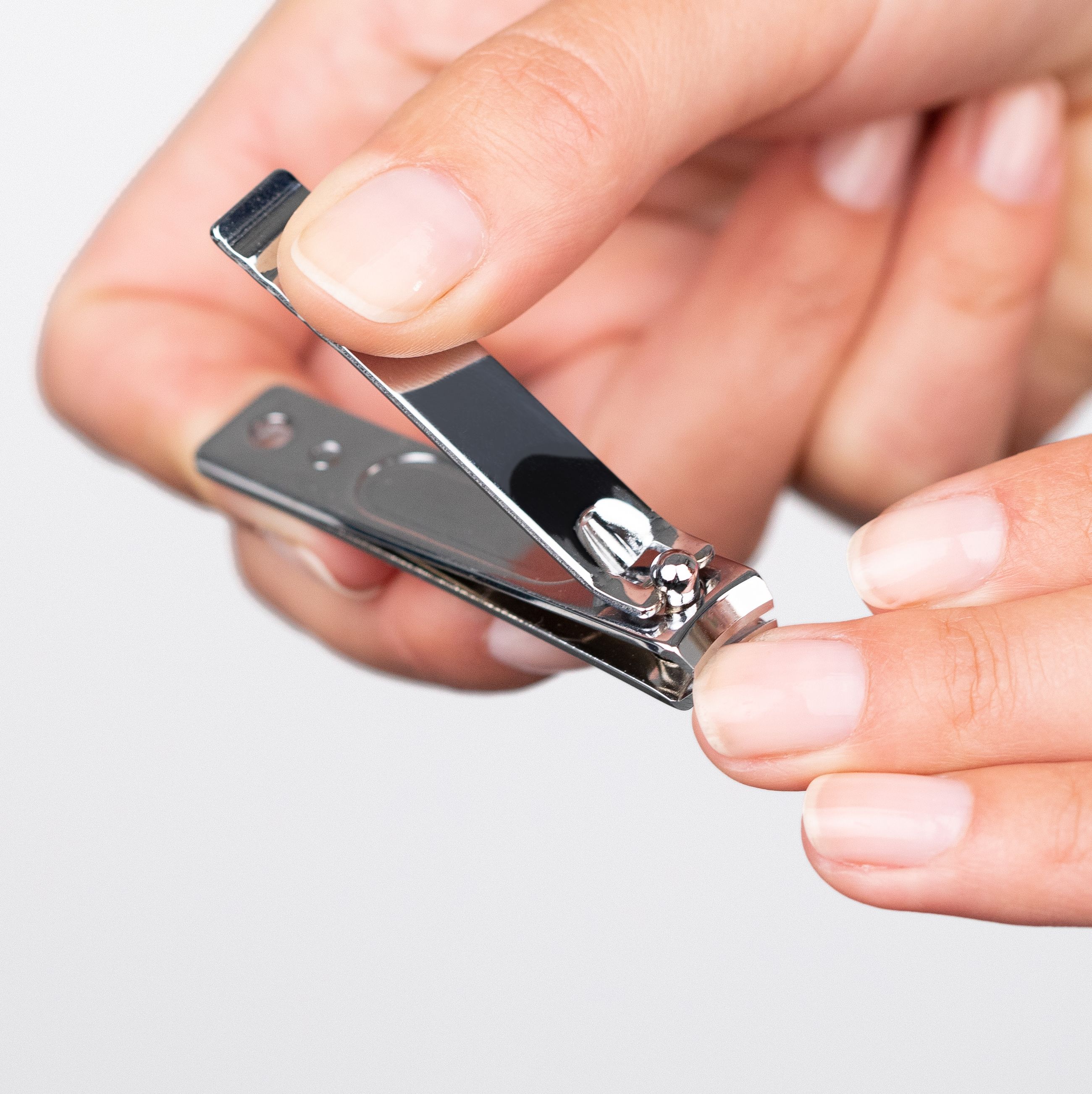 Nagelknipser in Gebrauch. Hände halten das Werkzeug. Schneiden eines Nagels. Glänzende Oberfläche.