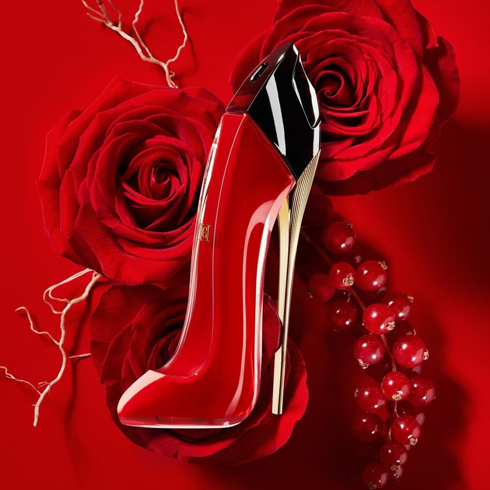 Roter High Heel-Flakon auf rotem Hintergrund mit Rosen und Beeren. Goldfarbene Sohle, schwarzer Deckel.