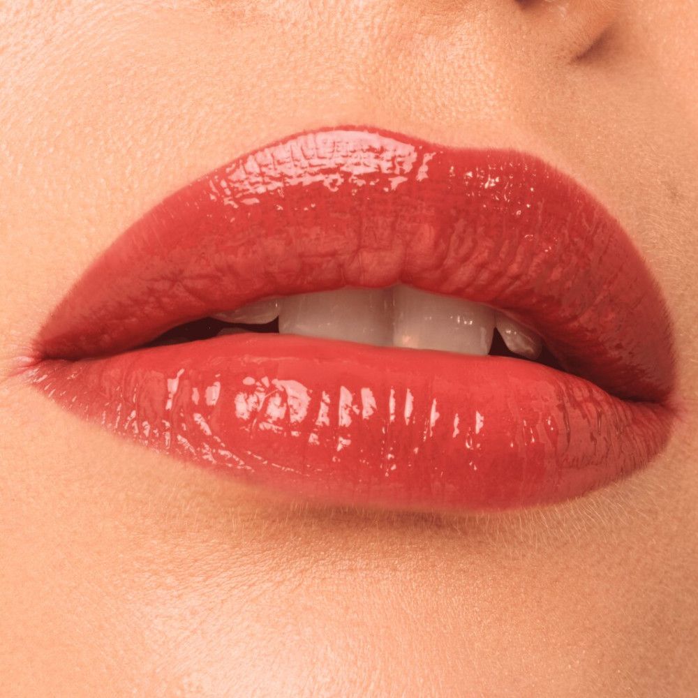 Nahaufnahme von Lippen mit glänzendem Lip Tint. Die Lippen sind rot gefärbt und leicht geöffnet, Zähne sichtbar.