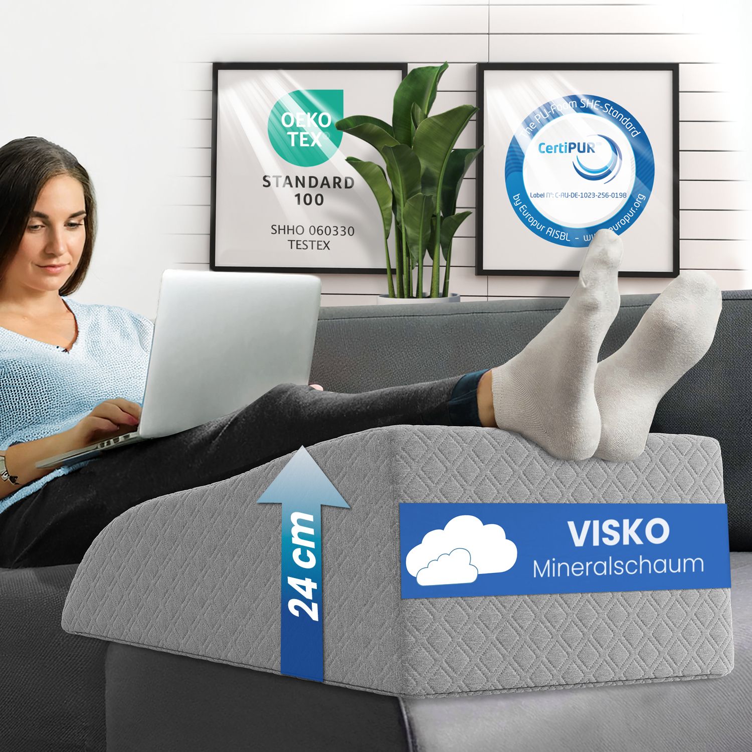 Frau sitzt auf einem Sofa mit einem grauen Beinlagerungskissen. 24 cm. Visko-Mineralschaum. Zertifizierungen.