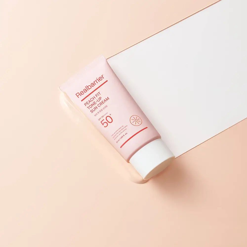 Rosa Tube mit weißem Verschluss. Aufschrift: Realbarrier Peach Fit Tone-Up Sun Cream LSF 50+ PA++++. Sonnenblumen-Symbol.