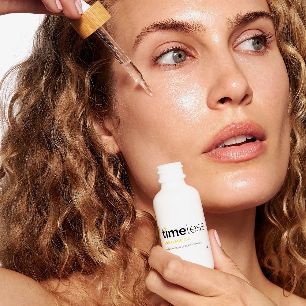 Frau trägt Öl mit Pipette auf die Haut auf. Weiße Flasche mit TIMELESS Squalane Oil-Aufschrift.
