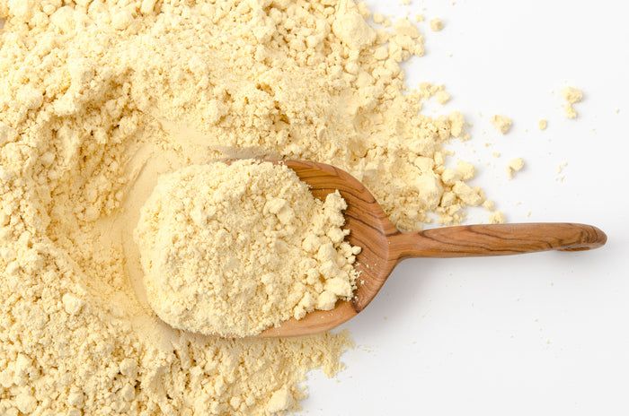 Haufen gelbes Pulver, daneben ein Holzlöffel mit Pulver. Auf weißem Hintergrund.