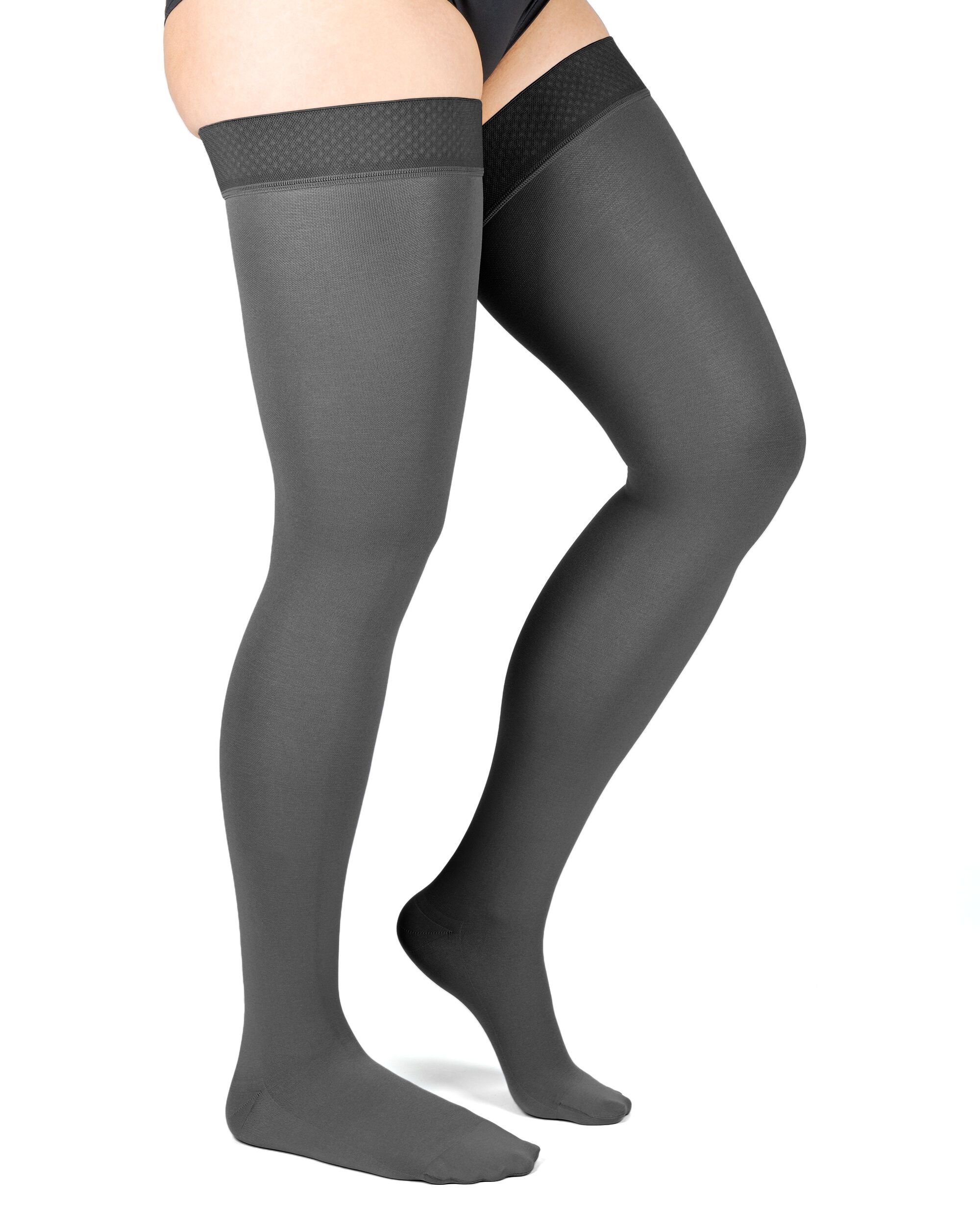 Graue Kompressions-Schenkelstrümpfe. Oberschenkelhoch, mit strukturiertem Abschlussband. Auf weißem Hintergrund, von der Seite.