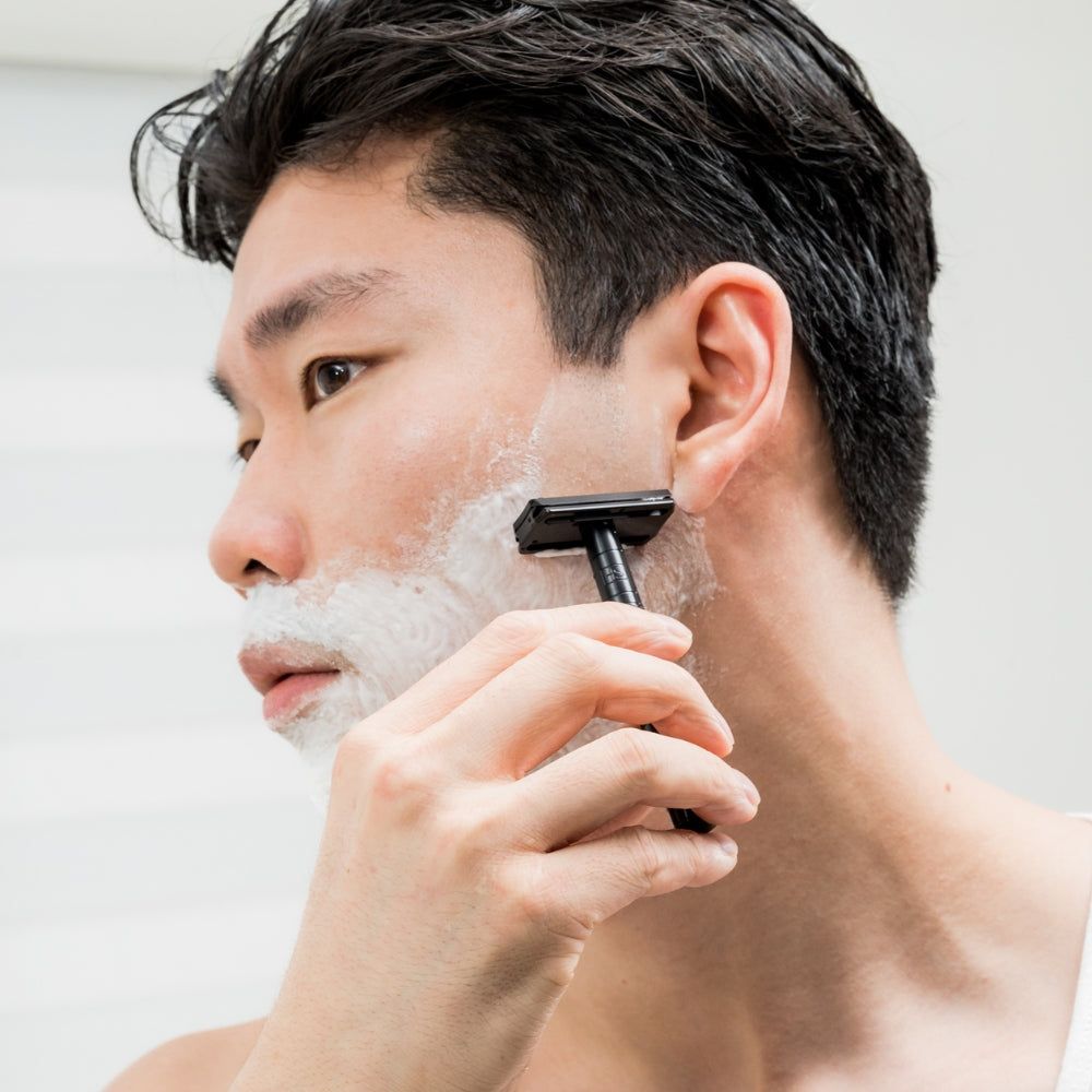 Mann rasiert sich mit schwarzem Rasierer. Schaum auf der Haut. Nahaufnahme.