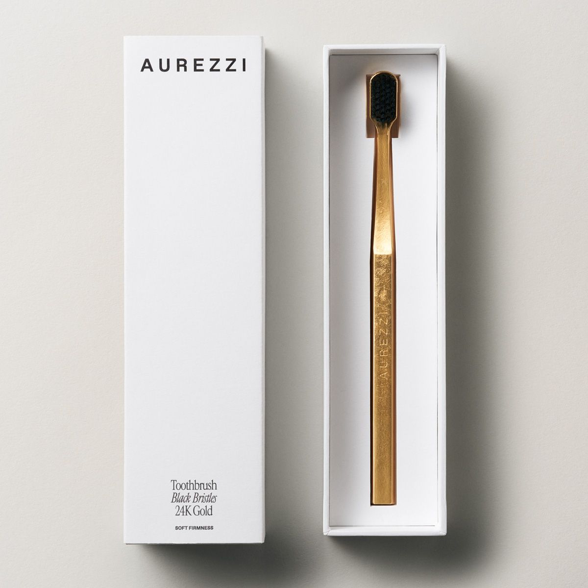 Zahnbürste Aurezzi Gold Schwarz, in weißer Schachtel. Auf der Schachtel steht "AUREZZI". Die Zahnbürste ist goldfarben.