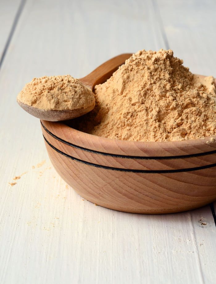 Holzschale mit Pulver und Löffel. Helles Pulver in einer Holzschale. Ein Holzlöffel liegt in der Schale.