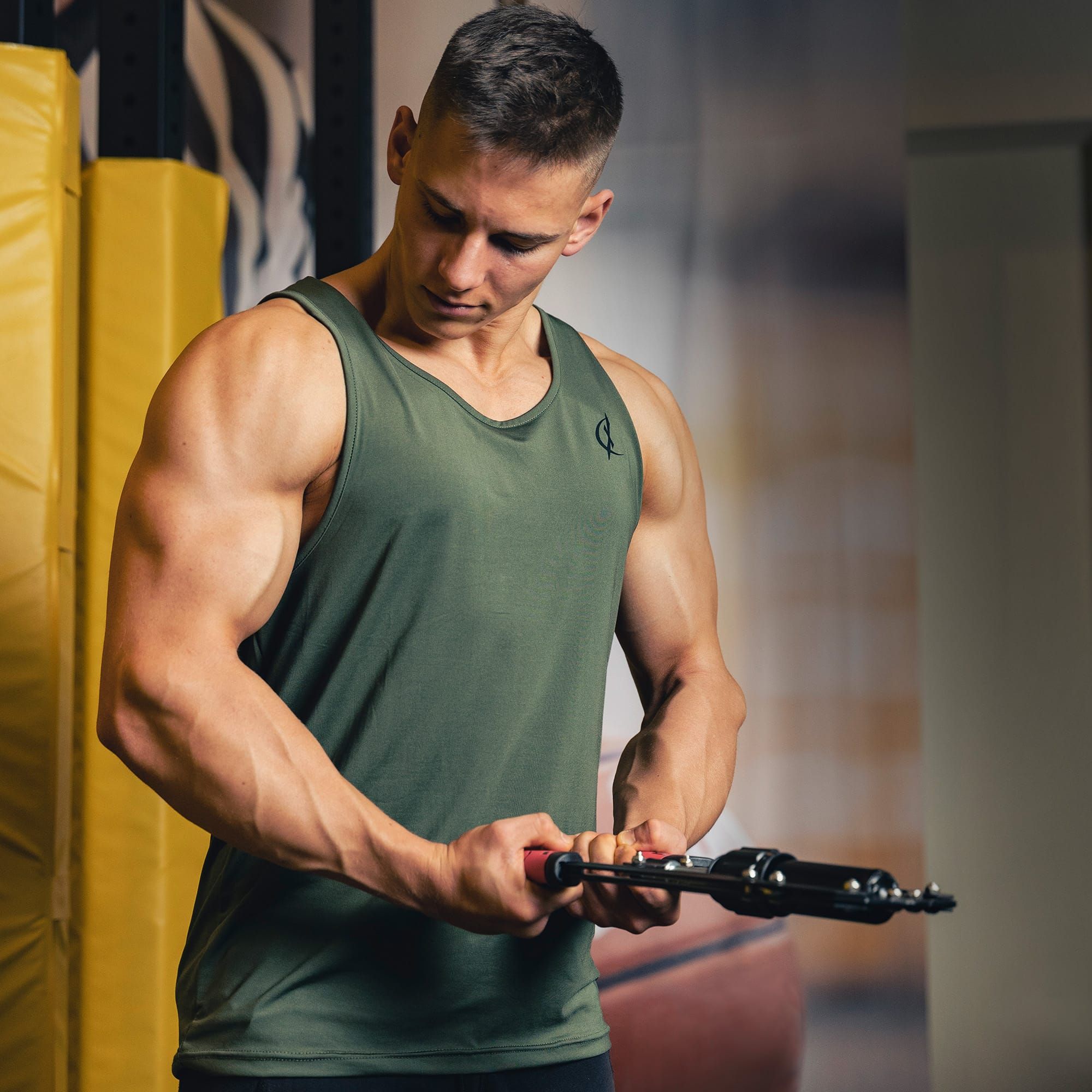Mann hält ein schwarzes Fitnessgerät. Er trägt ein grünes Tanktop. Nahaufnahme des Geräts.