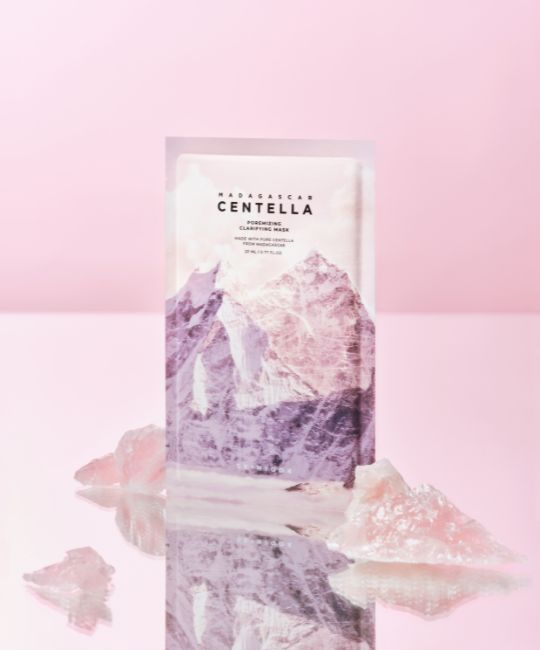 Gesichtsmaske mit Bergmotiv. Text: MADAGASCAR CENTELLA, Poremizing Clarifying Mask. Rosa Kristalle liegen davor.