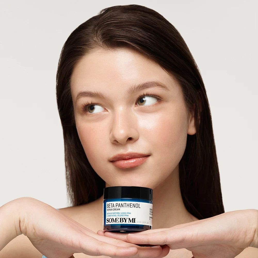 Eine Frau hält eine blaue Creme-Dose mit schwarzem Deckel. Auf der Dose steht "BETA PANTHENOL" und "SOME BY MI".