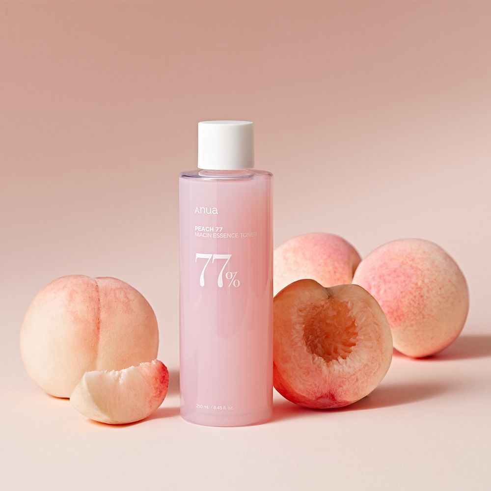 Flasche ANUA Peach 77% Niacin Essence Toner umgeben von Pfirsichen.