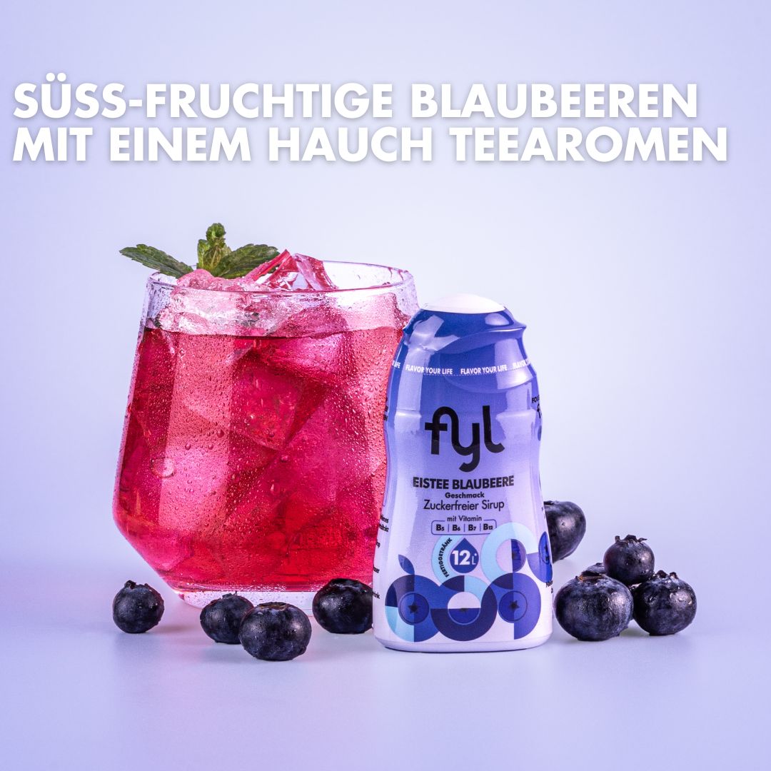 Glas mit Getränk und Eiswürfeln, daneben Flasche fyl Eistee Blaubeere. Blaubeeren liegen verstreut.