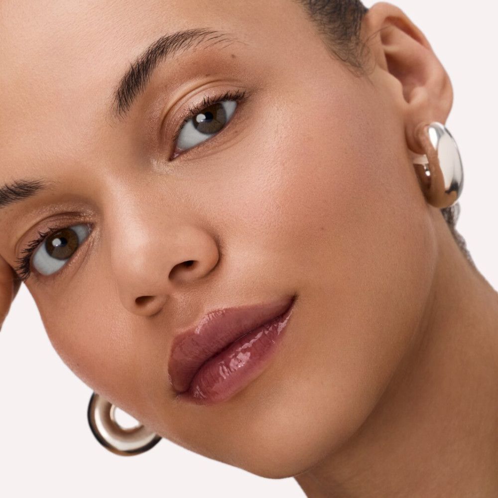 Nahaufnahme einer Frau mit glänzendem Lip Balm auf den Lippen. Goldene Ohrringe.