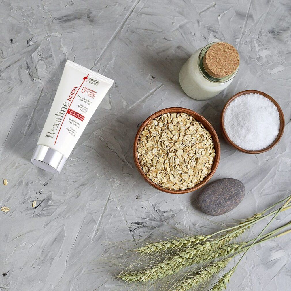 Produkt-Arrangement mit Creme-Tube, Haferflocken, Salz, Stein, Getreideähren und Glasbehälter mit Korken.