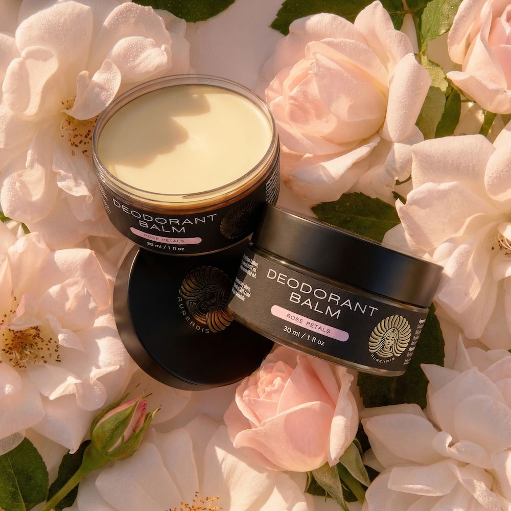 Zwei schwarze Tiegel Deobalm, geöffnet und geschlossen, auf Rosenblüten. Aufschrift: Deodorant Balm, Rose Petals.