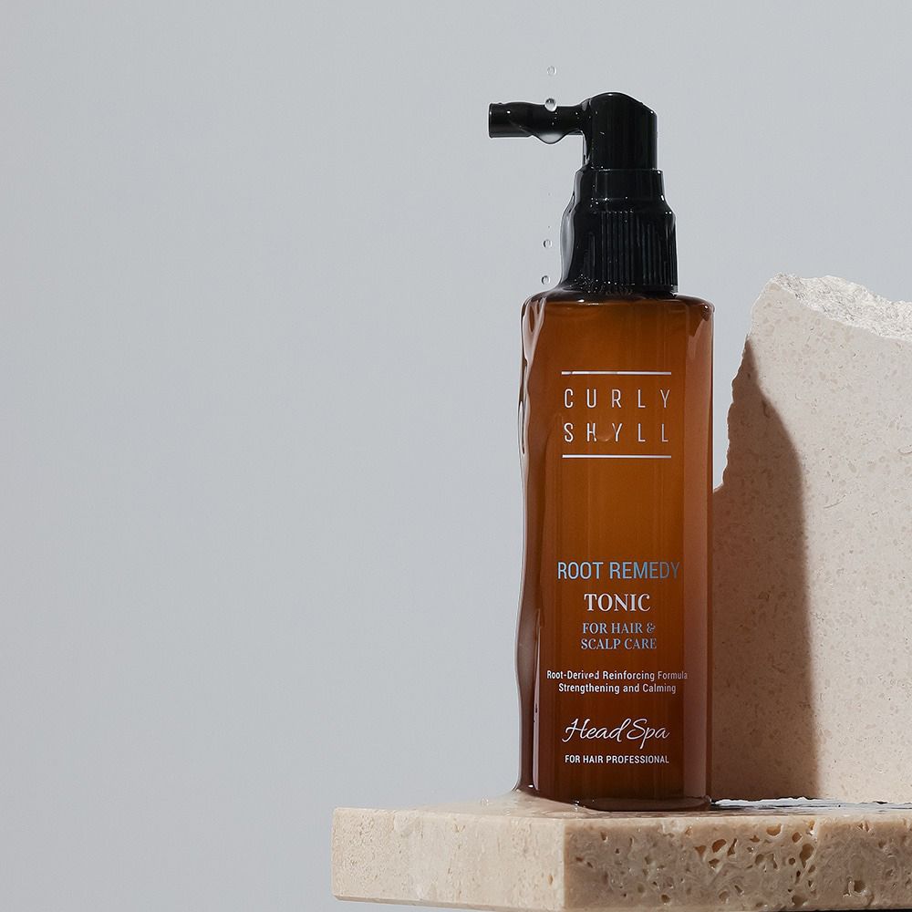 Braune Flasche mit schwarzem Sprühkopf. Beschriftung: CURLY SHYLL, Root Remedy Scalp Tonic, FOR HAIR & SCALP CARE. Wasserstrahl.