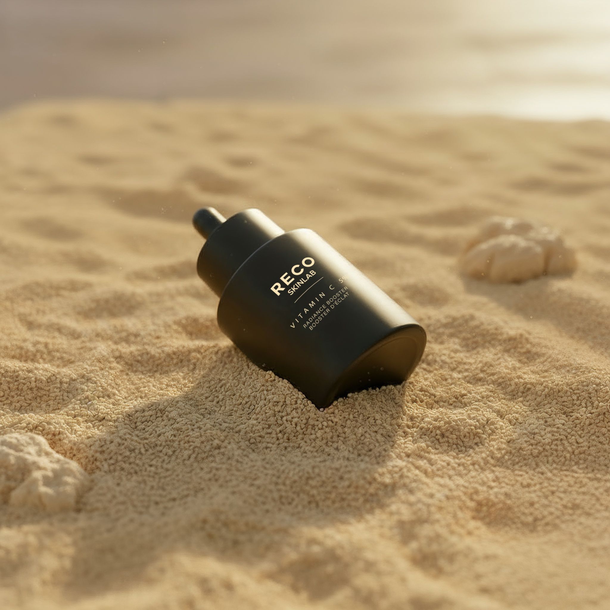 Schwarze Flasche auf Sand. Aufschrift: RECO SKINLAB, Vitamin C. Pipette nach oben gerichtet.