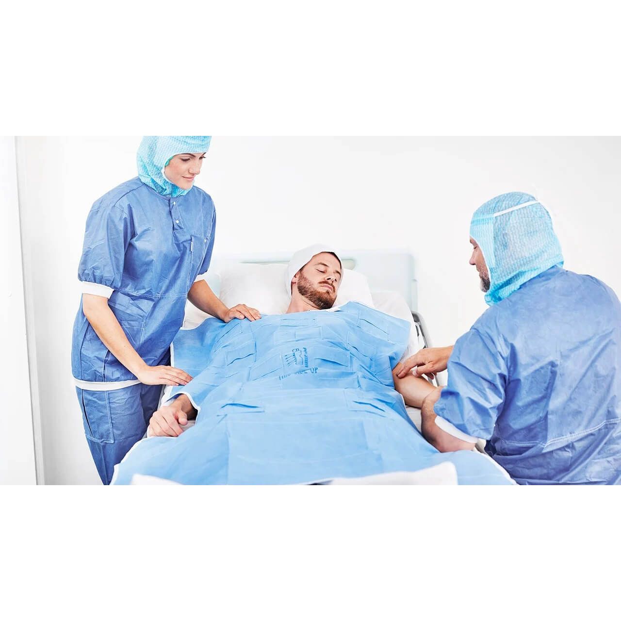 Patient im Krankenhausbett, bedeckt mit blauer Decke. Zwei medizinische Fachkräfte stehen daneben.