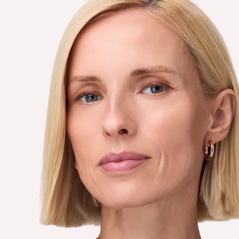 Porträt einer Frau mit blonden Haaren und rosafarbenen Lippen. Sie trägt Ohrringe.