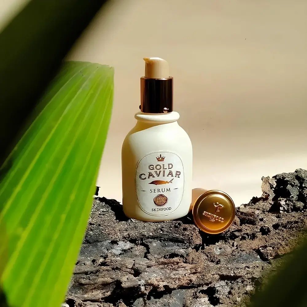 Serumflasche mit Deckel und Blatt. Text: Gold Caviar Serum. Marke: SKINFOOD. Hintergrund: Holz und Blätter.
