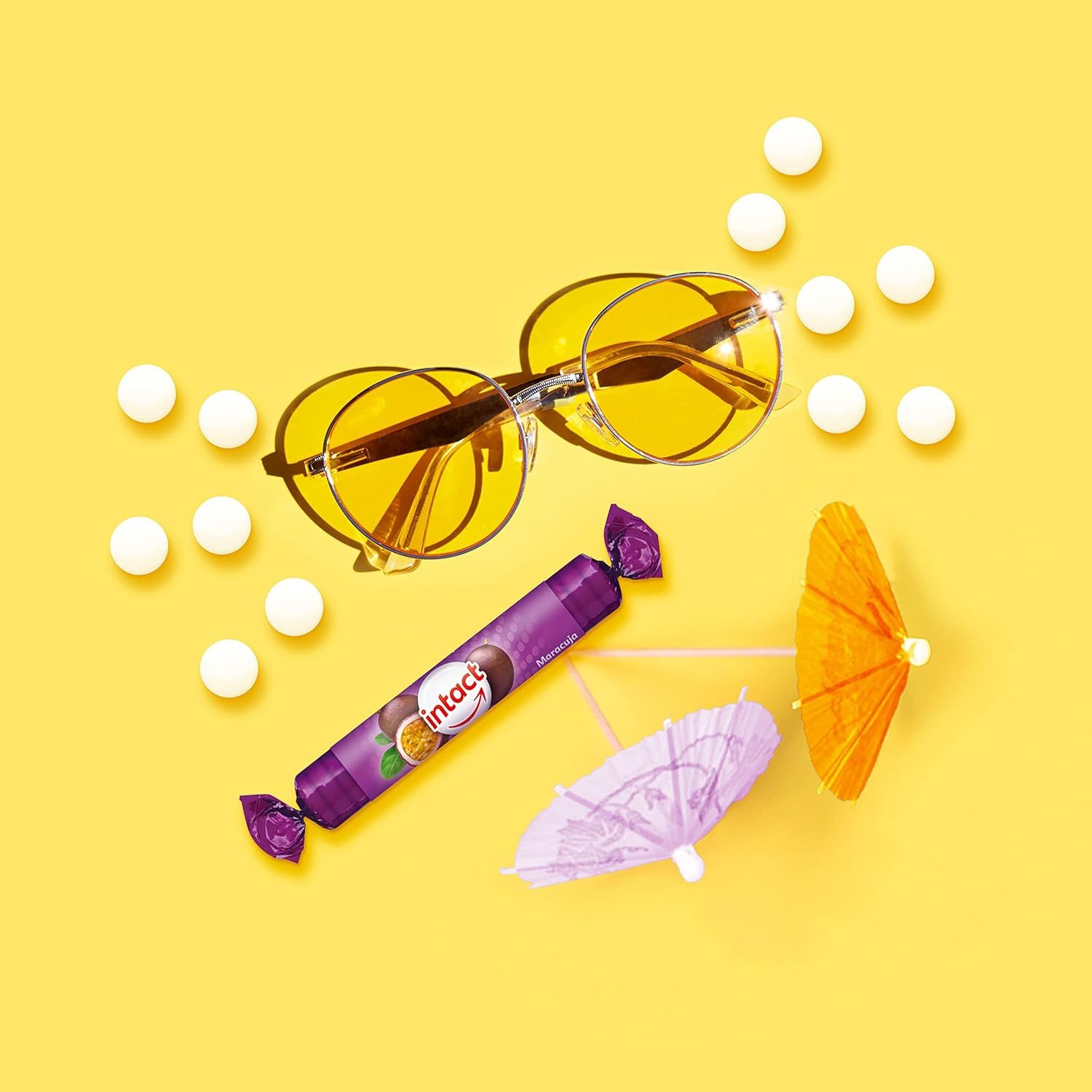 Eine Rolle Traubenzucker, Sonnenbrille und Sonnenschirme auf gelbem Hintergrund. Daneben weiße Tabletten.