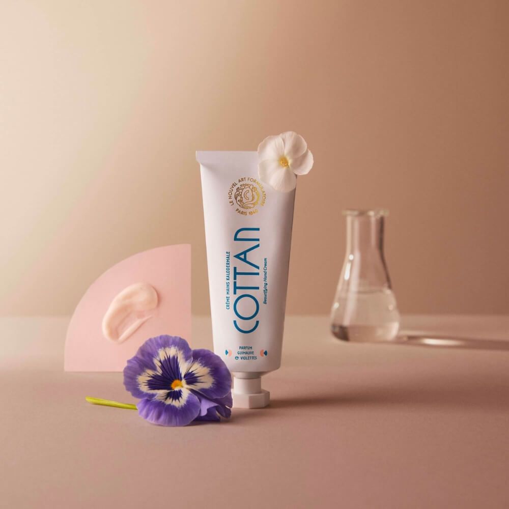 Weiße Tube COTTAN mit blauem Schriftzug, daneben eine rosa Form, eine Blume und ein Reagenzglas.