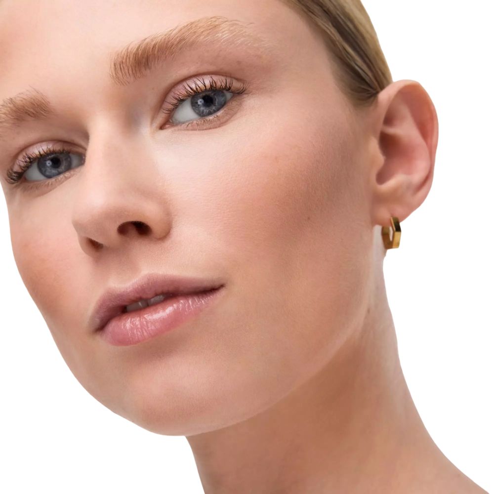 Porträt einer Frau mit blauäugigen Augen. Sie trägt goldene Creolen. Der Hintergrund ist weiß.